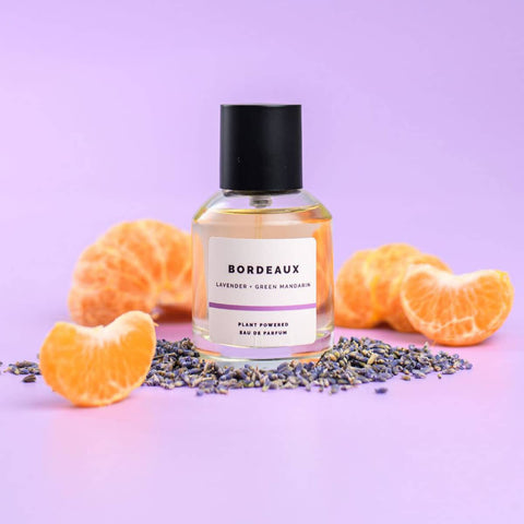 Bottle of ECO. Modern Essentials Bordeaux perfume with lavender & orange slices on a purple background.