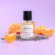 Bottle of ECO. Modern Essentials Bordeaux perfume with lavender & orange slices on a purple background.