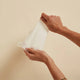 Person holding a baby wipe and stretching it to show tear-proof bamboo material. Set against a beige background.