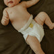 Baby wearing a white nappy on a dark olive bedspread.