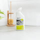 A bottle of ecostore Tough Oil & Lime Clean & Stain toilet cleaner stands on a light grey countertop in a bathroom setting, with a wooden brush holder and plant blurred in the background.