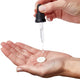 Hand holding a dropper with liquid over a white pill on a palm.