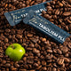 Two 'eMele Pro-TABOLISM PLUS' packets on coffee beans with a green apple.