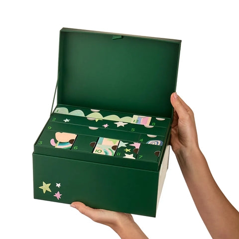 A dark green box held open by two hands against a solid white background. The box features multiple illustrated compartments with numbers and festive designs.