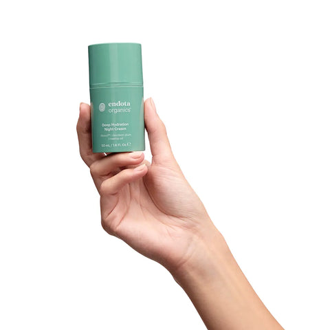 A hand holding a mint green cylindrical bottle of endota Deep Hydration Night Cream against a solid white background.