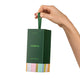 A hand holding a dark green Endota hair mask gift bag with a colourful striped pattern at the bottom, set against a plain white background.