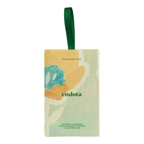 Endota lip duo packaged in a rectangular hanging box with a green ribbon loop. The packaging features a pastel design with abstract floral elements in yellow, orange, and teal on a light green background with small pink hearts.