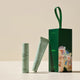 Endota Organic signature beauty set featuring a small roll-on bottle, a squeeze tube, and a dark green gift box with a floral print and carrying loop, arranged on a beige background.