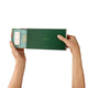 A person's hands holding open a dark green Endota travel diffuser kit box, revealing the inside against a solid white background.