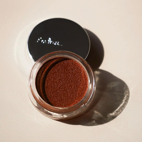 Open jar of Ere Perez Bronzing Pot -Costa 7.5g brown makeup product on a beige background.