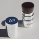 Ere Perez Kabuki Brush in retractable aluminium tube with lid and flat bottom for standing upright. Sitting on a grey surface with lid off.