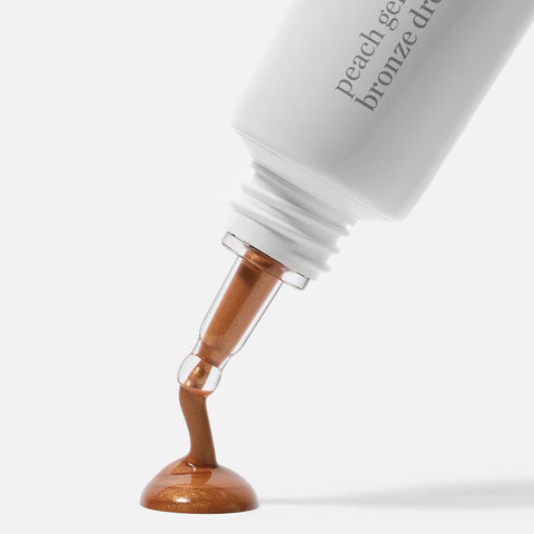 Close-up of a Ere Perez Peach Gel Bronze Drops 30ml product with a brown liquid being dispensed onto a white background.