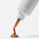 Close-up of a Ere Perez Peach Gel Bronze Drops 30ml product with a brown liquid being dispensed onto a white background.