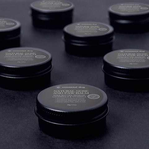 Multiple containers of 'essential dog' natural nose and paw balm on a dark surface.