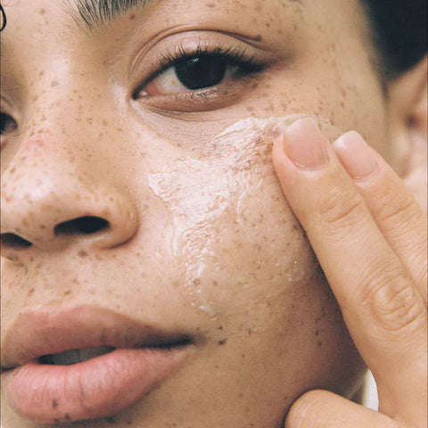 Close-up of a person applying skin butter to their cheek.
