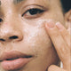 Close-up of a person applying skin butter to their cheek.