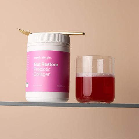 Jar labeled 'Gut Restore Prebiotic Collagen' 260g by Frank Simple next to a glass of red liquid on a beige background.