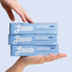 Three boxes of Grants Whitening +HA toothpaste held by a hand against a light blue background.