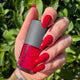Hand holding a red nail polish bottle with green foliage in the background