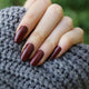 Hand with dark red nail polish on a textured gray surface