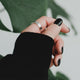 Hand with black nail polish and silver ring against a blurred green leaf background