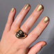 Hand with gold nail polish and a gold ring on a neutral background