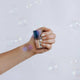 Hand holding a HANAMI nail polish bottle against a light background with bubbles.
