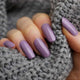 Hand with purple nail polish on a gray textured background