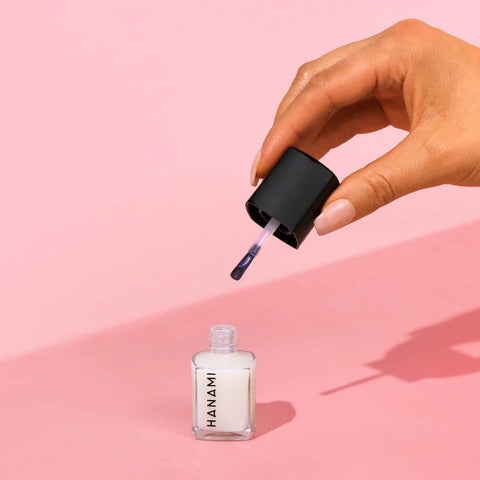 Hand applying Hanami nail polish to a pink background