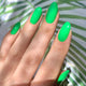 Hand with bright green nails against a leafy background