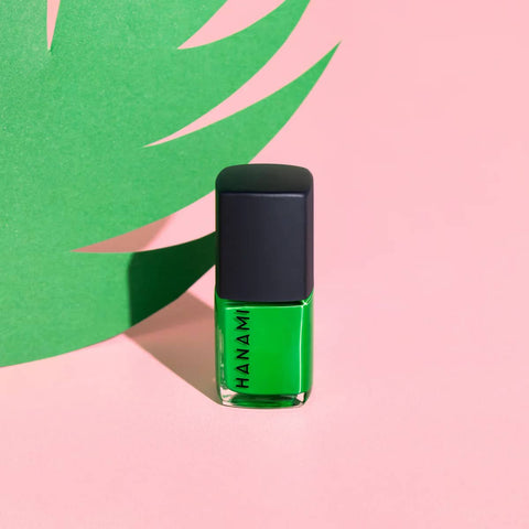 Green nail polish bottle with black cap on a pink and green background