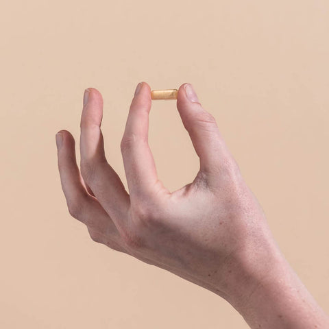 Hand holding a vitamin b capsule against a beige background