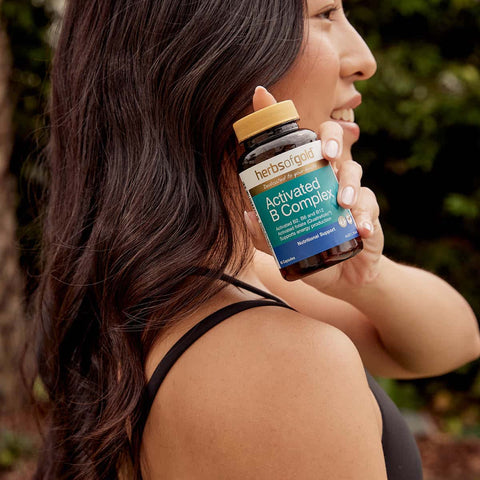 Woman holding a bottle of herbs of gold Activated B Complex supplement outdoors.