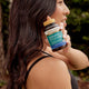Woman holding a bottle of herbs of gold Activated B Complex supplement outdoors.