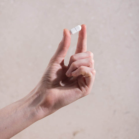 Hand holding a white magnesium tablet against a beige background