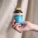 Hand holding a bottle of Herbs of Gold Vitamin D3 1000 against a neutral background.