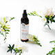 Essential scalp spray bottle with flowers on a white background.