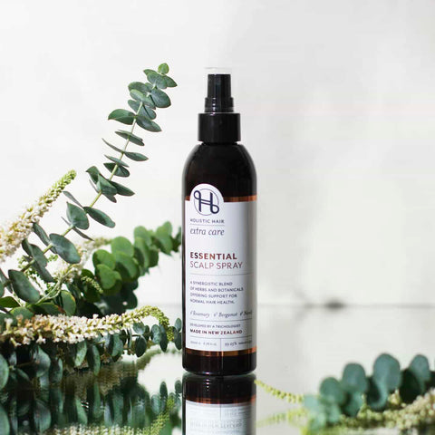 Bottle of essential scalp spray with eucalyptus leaves on a reflective surface.