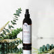 Bottle of essential scalp spray with eucalyptus leaves on a reflective surface.
