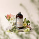 Bottle of herbal hair rinse with flowers and rocks on a blurred natural background.