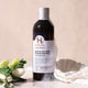 Bottle of Holistic Hair Colour Protect Shampoo with flowers and a white cloth on a beige background.