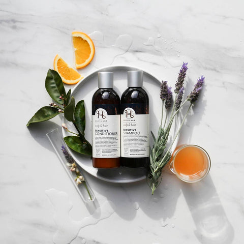 Two bottles of H&B hair care products on a white marble surface with lavender and orange slices.