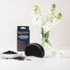 Black hairbrush with a bowl of black hair products and a vase of white flowers on a light background.