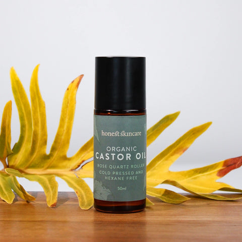 Honest Skincare Organic Castor Oil Rose Quartz Roller 50ml lifestyle shot of the bottle with its black cap on among yellow flowers and green leaves