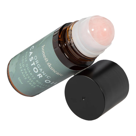 Honest Skincare Organic Castor Oil Rose Quartz Roller 50ml bottle lying on its side with the rose quartz roller ball and black cap beside it on white