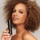 Woman with curly hair holding bottle of INIKA Organic Liquid Foundation.