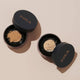 Two open black containers of INIKA Organic Loose Mineral Foundation on a beige background.