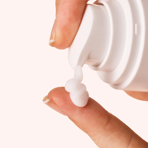INIKA Organic Pure Biome Hydro-Fluid Moisturiser 50ml lifestyle close up of a fingertip taking a dab of white cream from the pump bottle