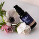 Bottle of rejuvenating oil leaning against some flowers on a light background. 