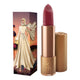 Lipstick next to box packaging that pictures a woman in a sparkling gold dress at sunset. Gold lipstick case with flower detail on lid. Natural, clean cosmetics.